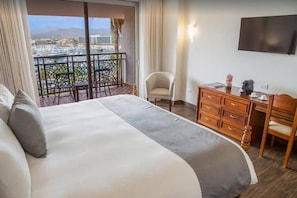 A hotel room with a large bed, a desk, a chair, and a view of a marina through a glass door. - 2BDFinisteria Resort Pool & Ocean Views (Cabo San Lucas)