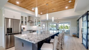 A modern kitchen with a large island, stainless steel appliances, and a view to the outside.