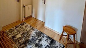 A hallway with a patterned rug, a wooden stool, and a radiator. - Birkenstr. 14 Wg.2 "timeout Oasis" - Entspannung Pur: Timeout Oasis Ferienwohnung in Strandnah (Zingst)