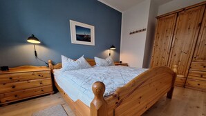 A wooden bed with a headboard, two bedside tables with lamps, a wooden wardrobe, and a framed picture on the wall. - Birkenstr. 14 Wg.2 "timeout Oasis" - Entspannung Pur: Timeout Oasis Ferienwohnung in Strandnah (Zingst)