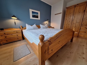 A wooden bed with a headboard, two bedside tables with lamps, a wooden wardrobe, and a framed picture on the wall.