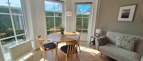 A room with a dining table, chairs, a sofa, and a view through large windows.