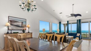 A spacious dining area with a large table and chairs, a chandelier, and a view of the ocean through large windows.