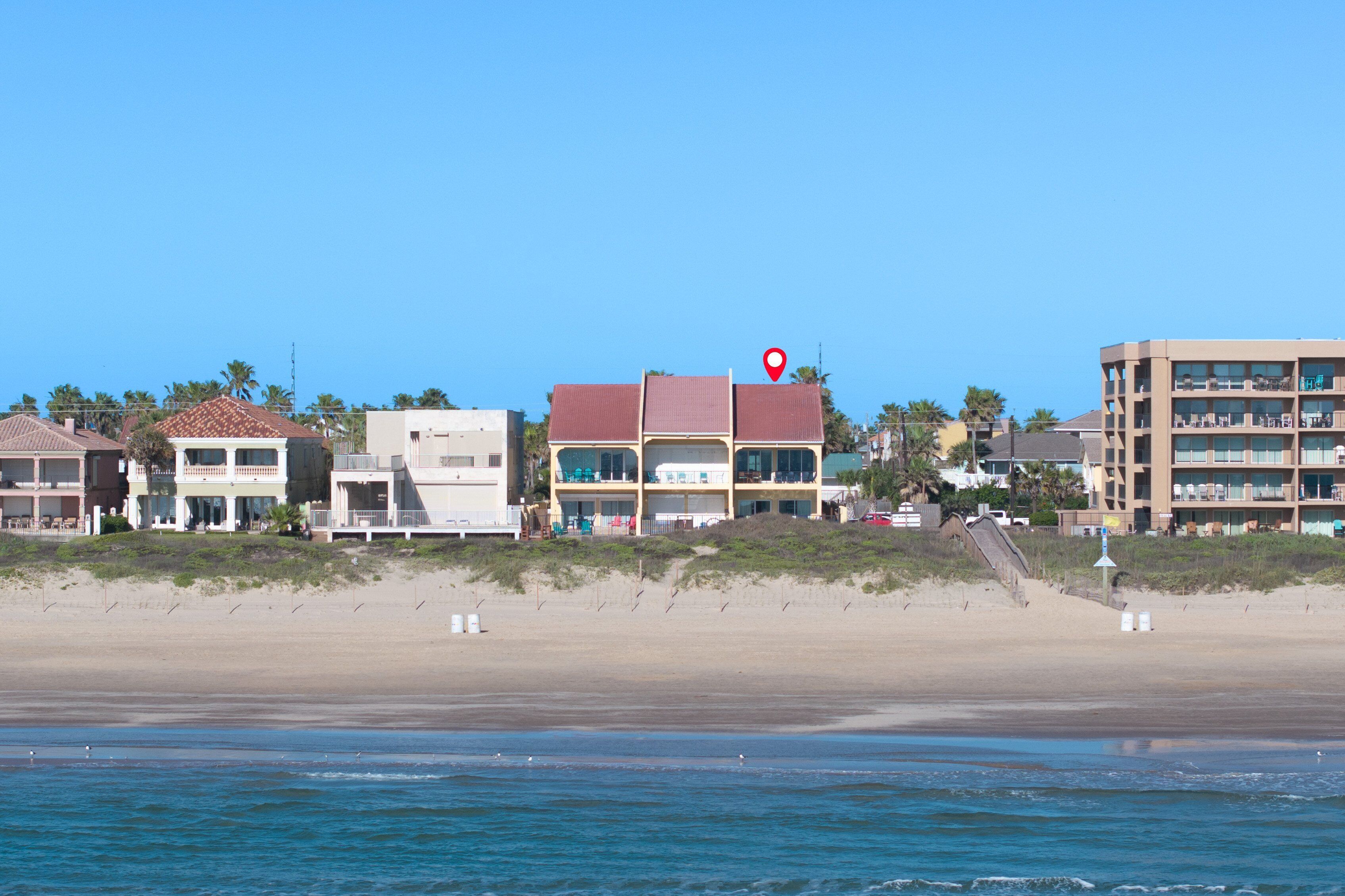 Un hotel sulla spiaggia con diversi piani, vista mare e un segnaposto rosso.
