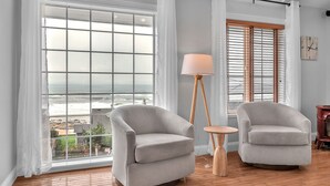 A room with two grey armchairs, a floor lamp, and large windows with a view of the ocean. - Ocean View Haven - Walk to the Beach (Lincoln City)