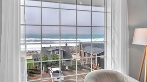 A room with a large window overlooking a beach, a chair, and a lamp. - Ocean View Haven - Walk to the Beach (Lincoln City)
