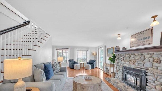 A spacious living room with a stone fireplace, a staircase, and a view of the outdoors. - Ocean View Haven - Walk to the Beach (Lincoln City)