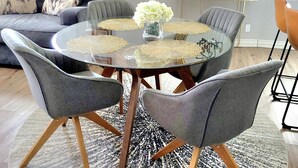 A dining area with a round glass table, grey upholstered chairs, and a vase with white flowers.