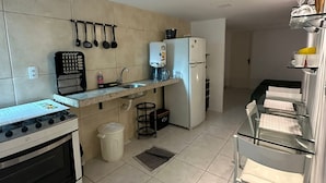 A modern kitchen with a gas stove, a refrigerator, and a sink. There are hanging utensils and a coffee machine. - Beach Flats Porto de Galinhas (Ipojuca)