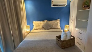 A bedroom with a bed, a bedside lamp, an air conditioning unit, and a wardrobe. - Beach Flats Porto de Galinhas (Ipojuca)