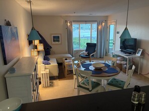 A cozy living room with a sofa, a dining table with chairs, a television, and a window with curtains.