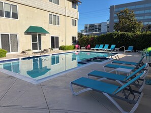 A swimming pool with lounge chairs and a building in the background.