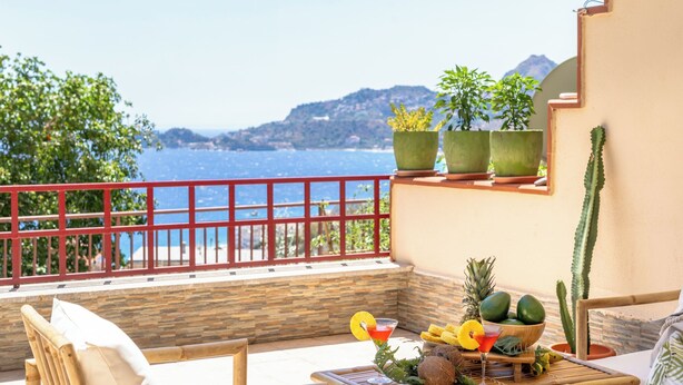 A balcony with a view of the sea, a table with fruits and drinks, and a cactus plant. - Seabreeze Boho Stay - Apartment with sea view (Letojanni)