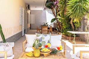 A cozy outdoor seating area with a wooden table set with tropical fruits, a cocktail, and a hat. - Seabreeze Boho Stay - Apartment with sea view (Letojanni)