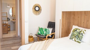A bedroom with a wooden headboard, a bed with white bedding, a chair with a green leaf pillow, and a wall-mounted mirror. - Seabreeze Boho Stay - Apartment with sea view (Letojanni)