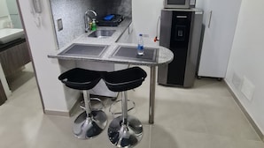 Une cuisine moderne dotée d’un plan de travail en granit, de deux tabourets de bar noirs, d’un four à micro-ondes encastré et d’un réfrigérateur.