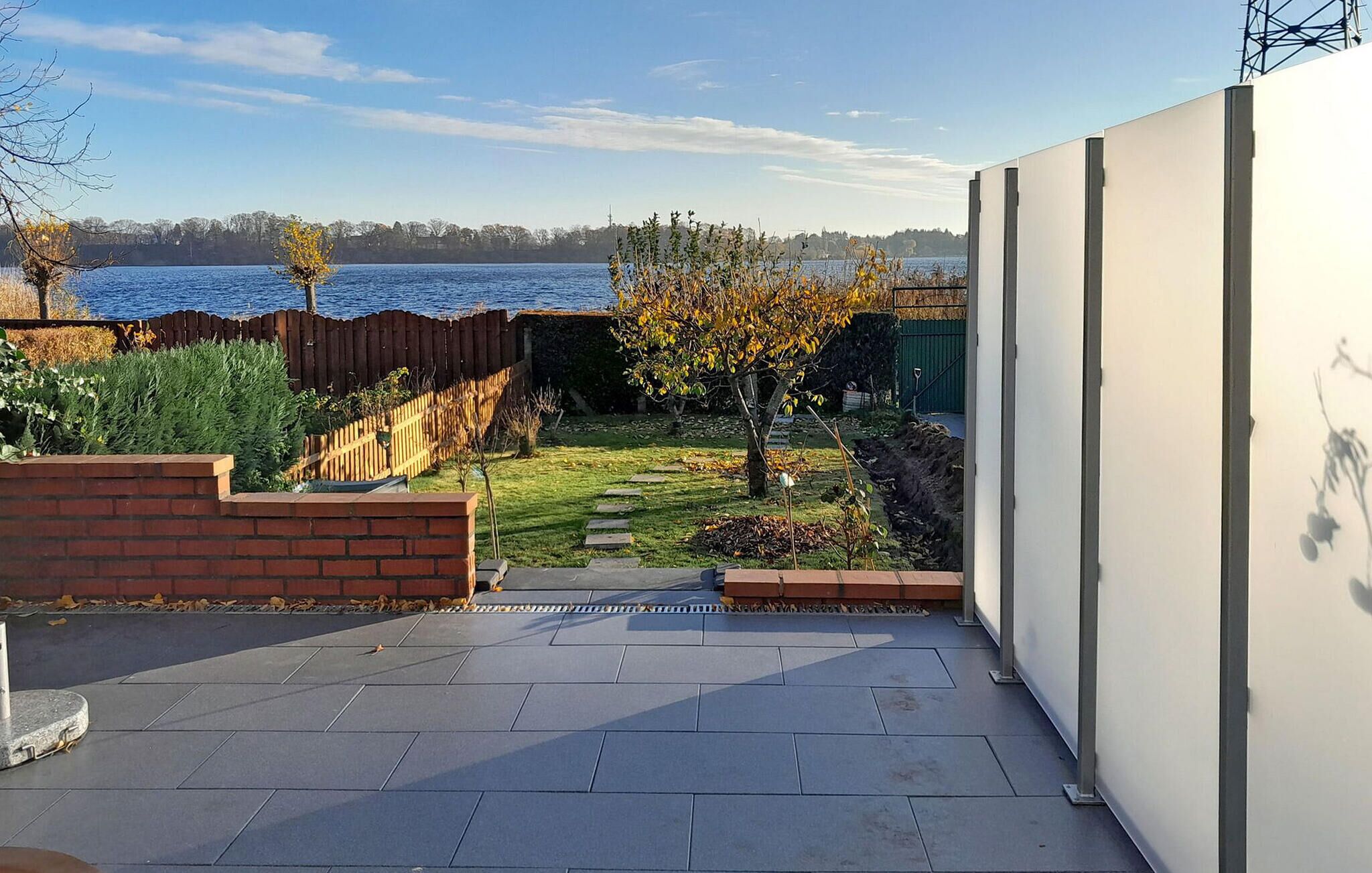 Eine Terrasse mit Blick auf einen See, eine Ziegelmauer und ein Holzzaun.
