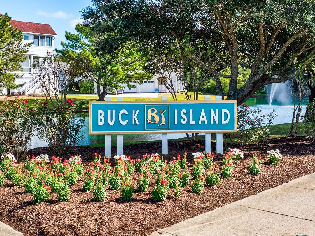 A sign for Buck Island with a view of a house and a fountain in the background.