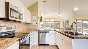 A modern kitchen with white cabinets, granite countertops, stainless steel appliances, and a large island with a sink. - Beachin Fun (South Unit) | 1665 ft to the beach | Hot Tub, Dog Friendly, and Community Pool (Corolla)