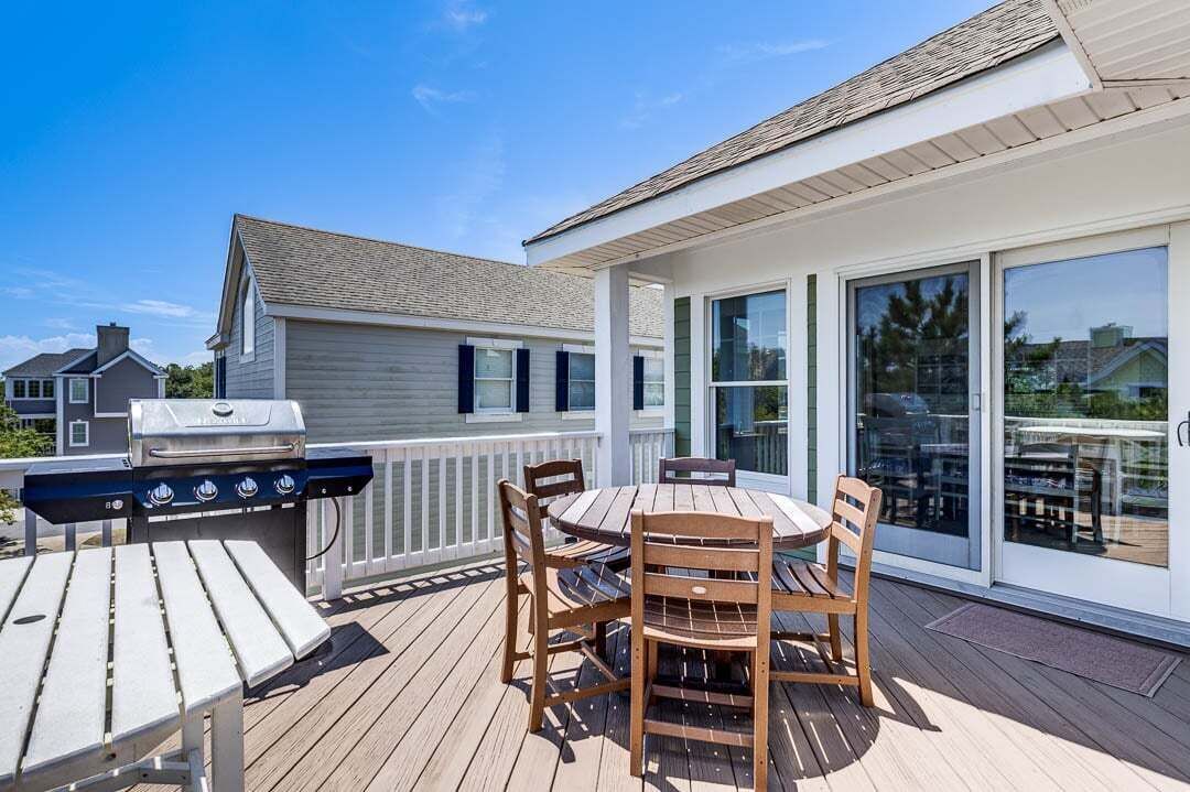 A deck with a grill, a round table, and chairs.