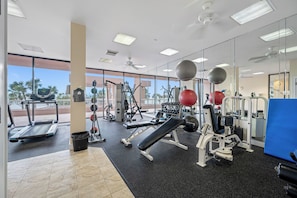 A gym with various exercise equipment, a treadmill, and a large window offering a view of palm trees.