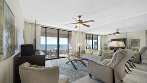 A spacious living room with a large sliding glass door leading to a balcony, a ceiling fan, and a television on a stand.