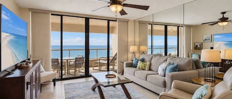 A spacious living area with a balcony overlooking the ocean, furnished with a sofa, coffee table, and lamps.