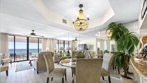 A spacious living area with a large chandelier, comfortable seating, and a view of the ocean.
