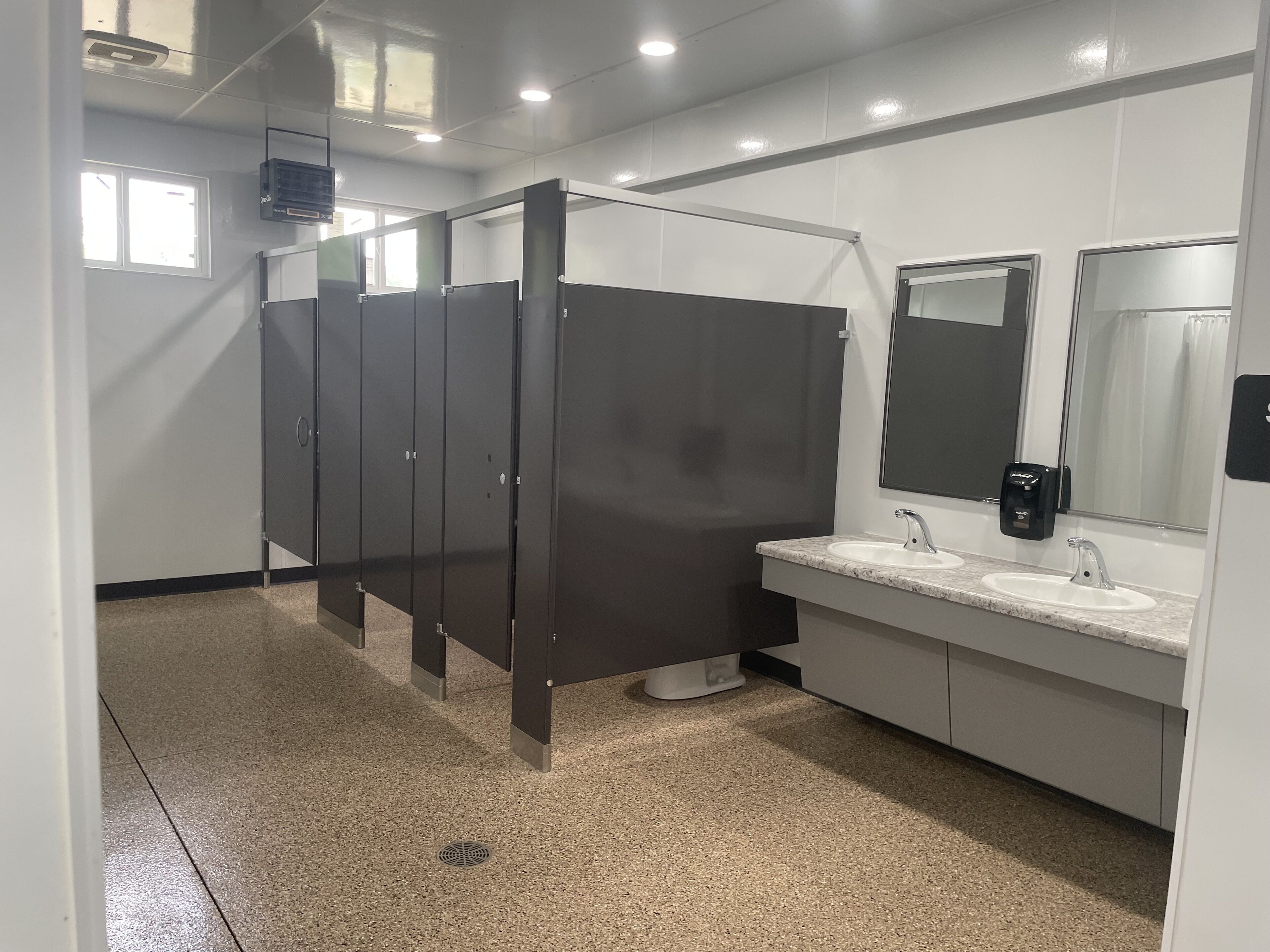 A modern bathroom with a row of dark stalls, a sink with a mirror, and a hand dryer.