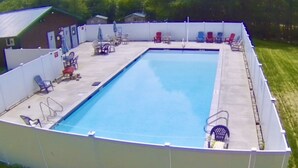 A rectangular swimming pool with a white deck, surrounded by a white fence. There are lounge chairs and a table with umbrellas on the deck. - Rustic Sleeping Cabin #14, sleeps up to 12 guests,  No Water in Cabin (Letts)