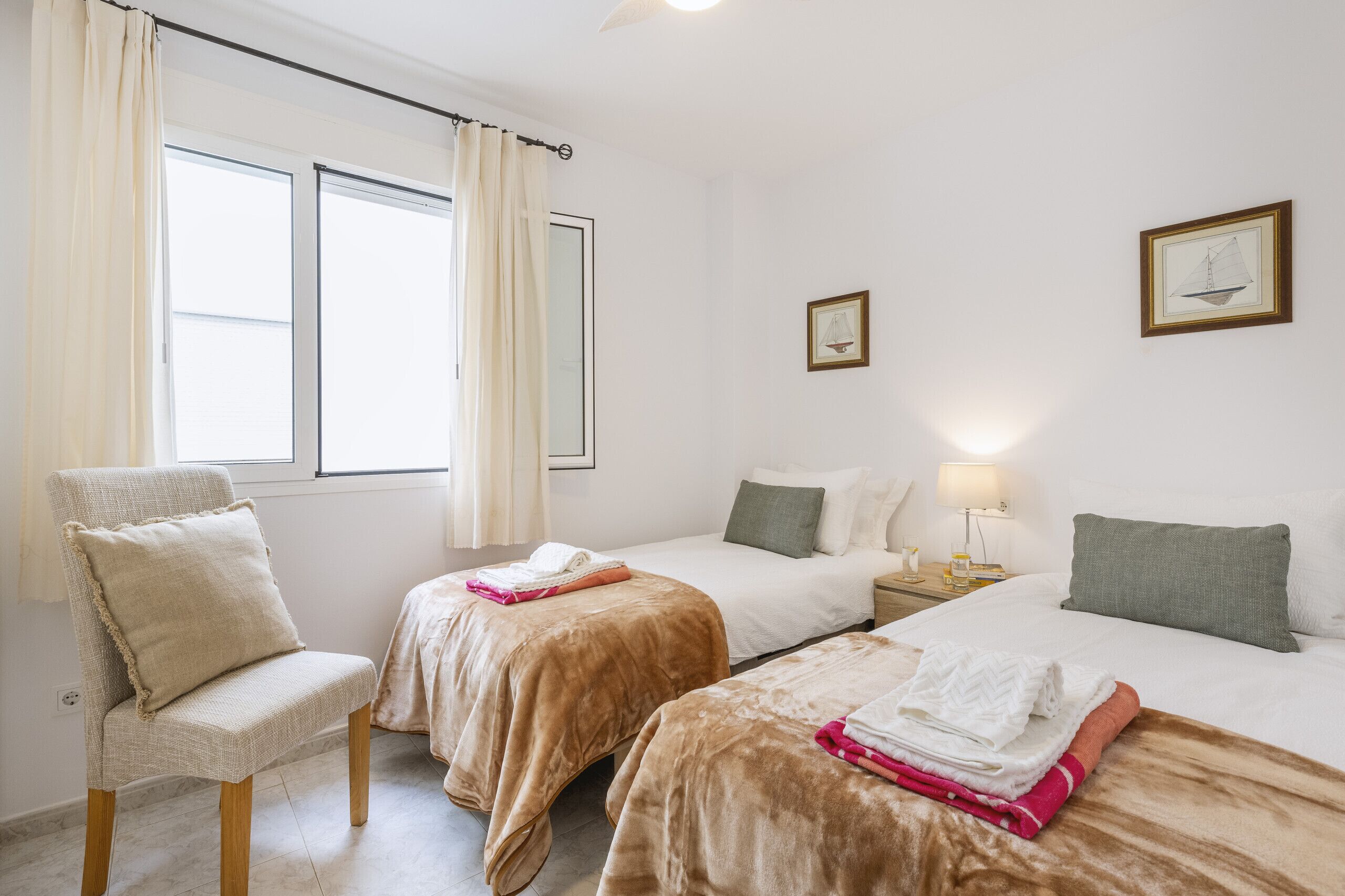 Habitación de hotel con dos camas, una silla, una mesita de noche y una ventana con cortinas.