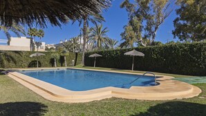 A swimming pool with a curved edge, surrounded by grass and palm trees.