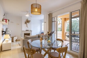 Relax in this open-plan living space with a glass dining table, fireplace, and large window offering a view of the outdoor area.
