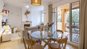 A modern living room with a glass dining table, comfortable seating, a fireplace, and a balcony with outdoor furniture.