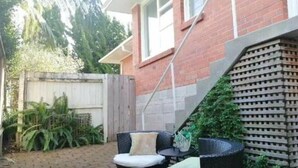 Un patio con mobiliario de mimbre, cerca de madera y casa de ladrillo.