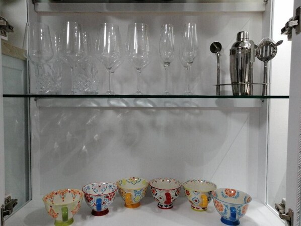 Une étagère avec des verres à vin transparents et un ensemble de bols colorés.