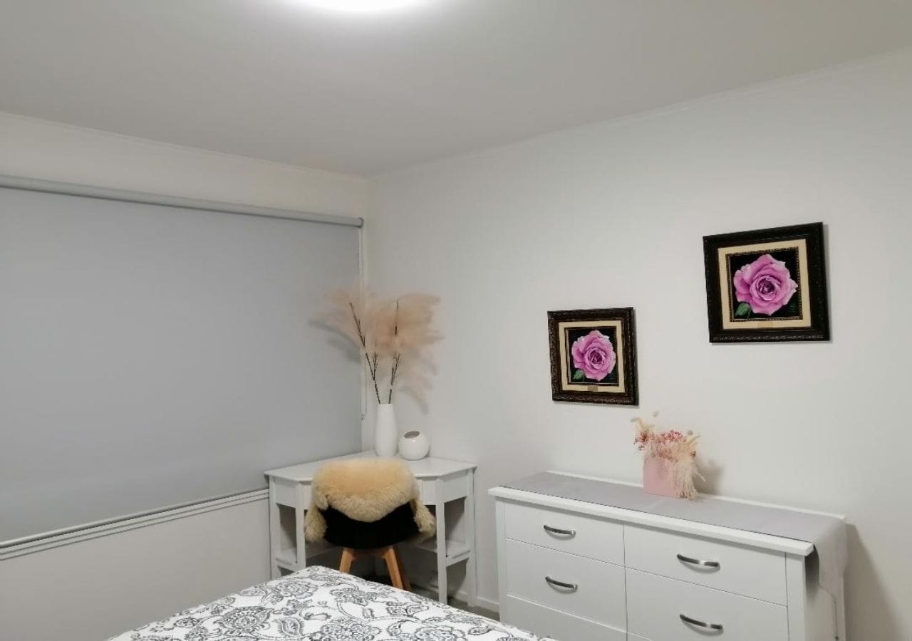 A bedroom with a bed, a desk, a chair, and a dresser. There are two framed pictures on the wall.