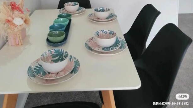 Una cocina moderna con armarios blancos, un ventanal con vistas a un jardín y una zona de comedor con una mesa blanca dispuesta para cuatro comensales.