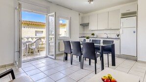 A modern kitchen with white cabinets, a dining area with black chairs, and a balcony with white chairs. - Apartment Muga by Interhome (Empuriabrava)