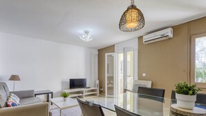A modern living room with a glass dining table, comfortable seating, a flat-screen TV, and a ceiling light fixture. - Apartment Muga by Interhome (Empuriabrava)