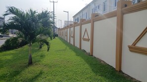 A pathway lined with palm trees and a building with a beige exterior and triangular window designs.