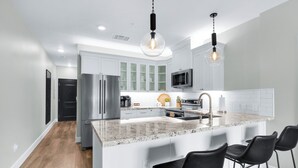 A modern kitchen with white cabinets, stainless steel appliances, a granite countertop, and black bar stools.