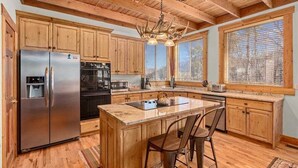 A spacious kitchen with wooden cabinets, a stainless steel refrigerator, a large island with bar stools, and a hanging light fixture. - SUN RIDGE - 6 BD, VIEWS, POOL TABLE, HOT TUB (Sundance)