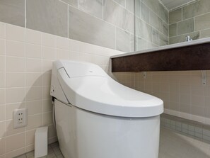 A modern bathroom with a white toilet, a small trash bin, and a mirror above the sink.