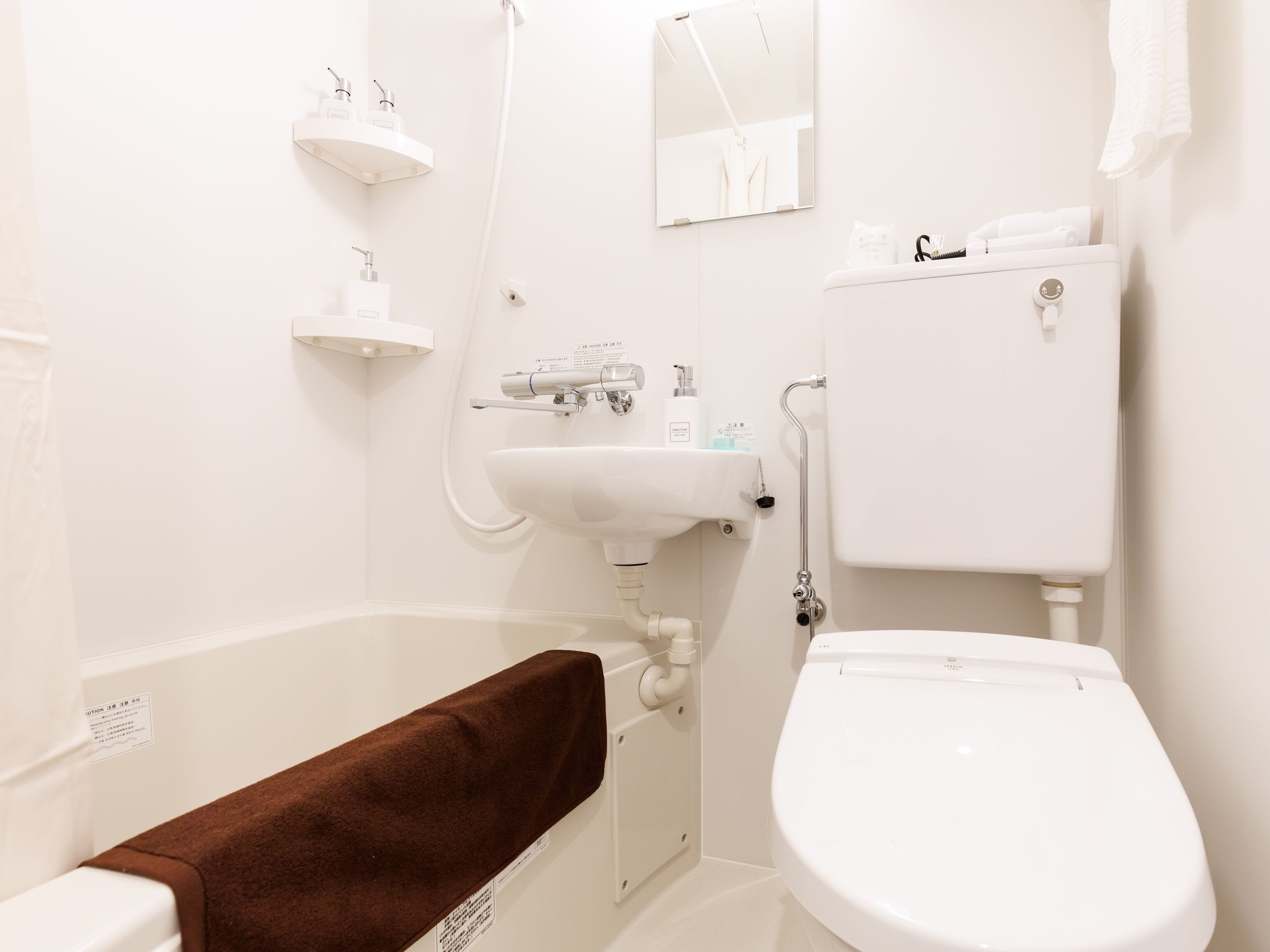 Un baño con lavamanos, inodoro y bañera blancos. Hay estantes blancos con artículos de aseo y un perchero.