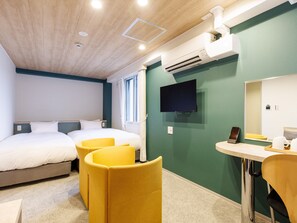 A hotel room with two beds, a desk, a chair, a TV, and an air conditioning unit.