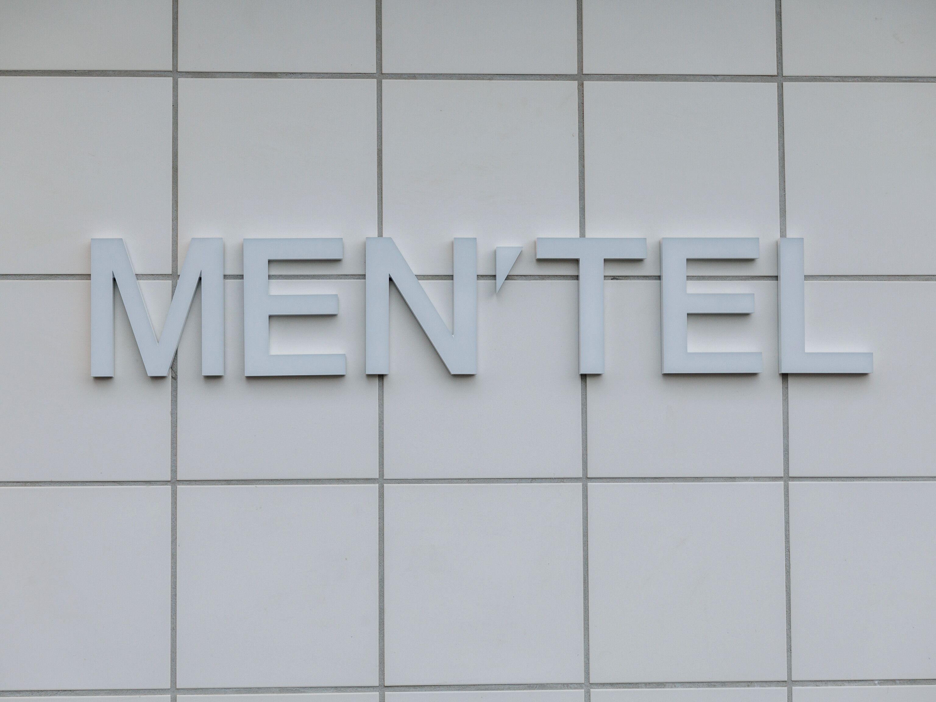 A white tiled wall with the word "MEN'TEL" in large, capital letters.
