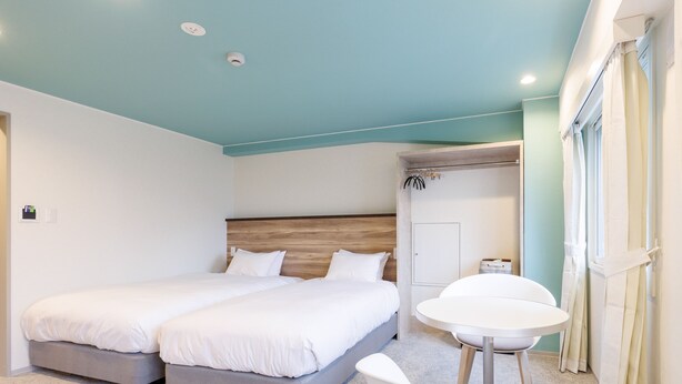 Une chambre d’hôtel moderne avec deux lits, une baignoire blanche, une table ronde et une porte donnant sur la salle de bain.