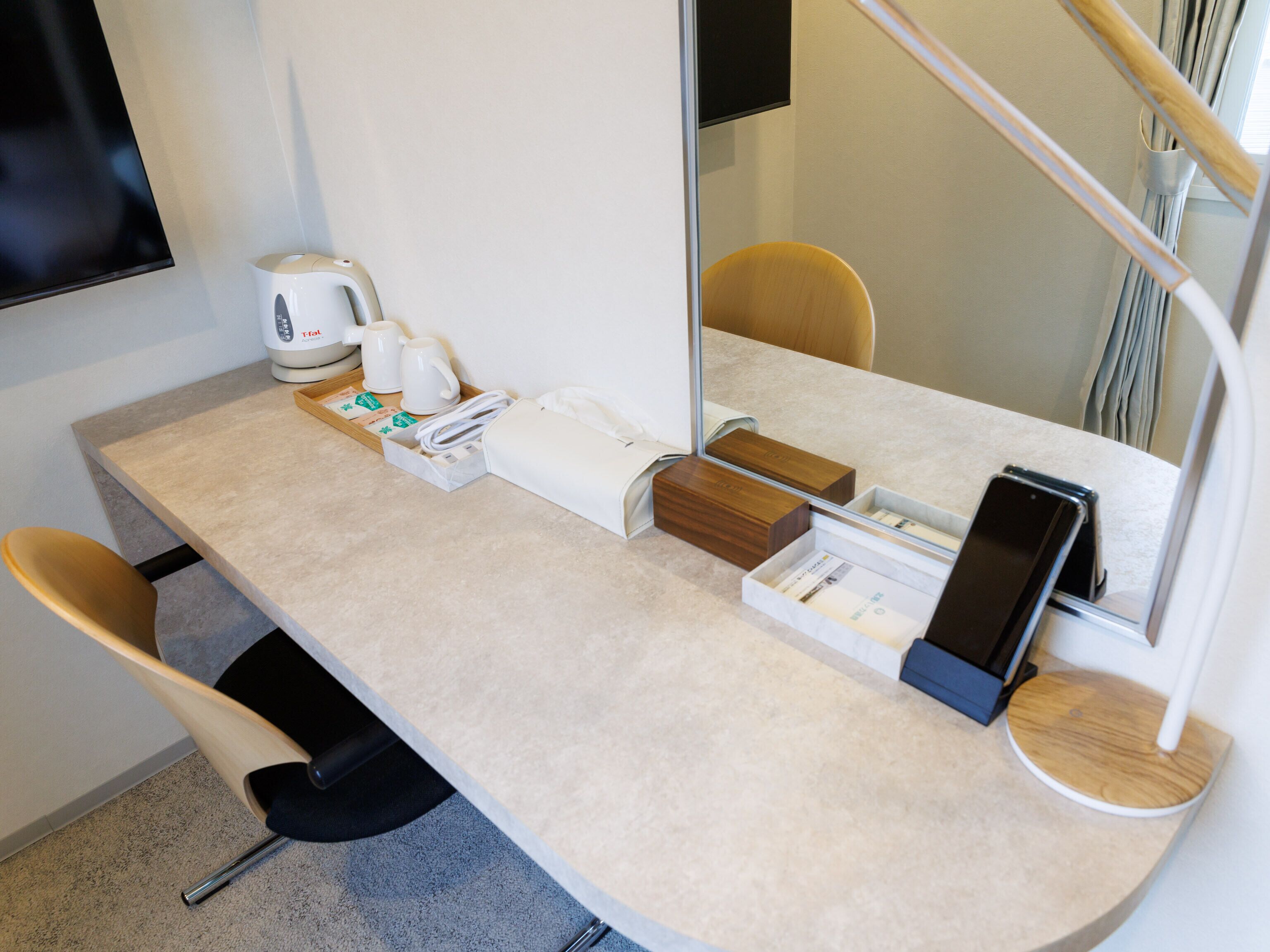 A hotel room with a curved desk, a coffee maker, a smartphone charging station, and a mirror.