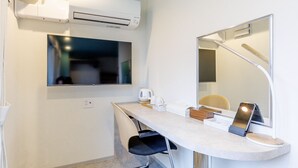Une chambre d’hôtel moderne dotée d’un bureau incurvé, d’un téléviseur à écran plat, d’un climatiseur, d’un miroir et d’une lampe de bureau.